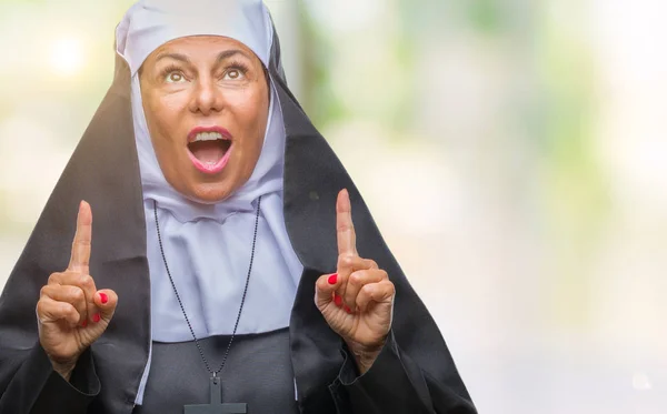 孤立した背景に中年シニア キリスト教カトリック修道女女性びっくりと驚いて見上げると指で指していると腕を上げた — ストック写真