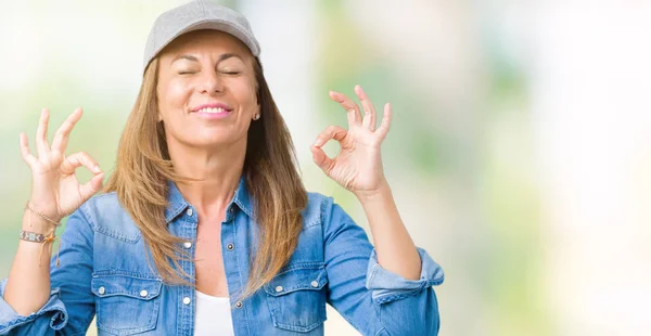美丽的中年妇女戴着运动帽在孤立的背景放松和微笑与眼睛闭着做冥想手势用手指 瑜伽概念 — 图库照片