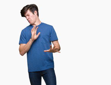 İzole arka plan üzerinde mavi t-shirt giyen genç yakışıklı adam tiksinti ifadesi, memnun ve korkulu tiksinti yüz yapıyorsun çünkü nefret tepki. Elleriyle kaldırdı. Sinir bozucu kavramı.