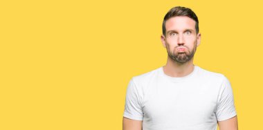 Komik surat ile rahat beyaz t-shirt şişirme yanakları giyen yakışıklı adam. Ağız ile hava, deli ifade şişirilmiş.