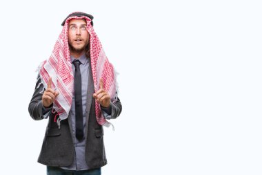 Genç yakışıklı Arap adam uzun saçlı keffiyeh izole arka plan üzerinde giyen hayrete ve yukarıya bakıyor ve parmakları ile işaret ve silah kaldırdı şaşırttı.