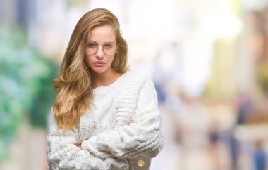 Kış kazak ve güneş gözlüğü izole arka plan şüpheci ve sinir, onaylamayan ifade yüz çapraz kolları üzerinde giyen genç güzel sarışın kadın. Negatif kişi.