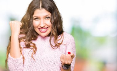 Kutlayan pembe kazak giyen genç güzel kadın şaşırttı ve başarı için kaldırdı kollarını açarak hayret ve gözleri açık. Kazanan kavramı.