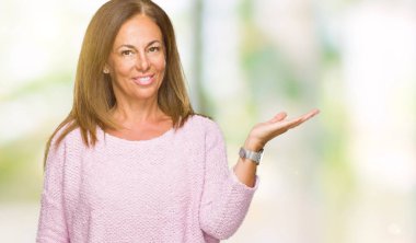 Neşeli sunulması ve kameraya bakarak avucunun ile işaret gülümseyen izole arka plan üzerinde kış kazak giyen güzel orta yaş yetişkin kadın.