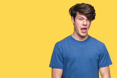 Seksi bir ifadeyle, neşeli ve mutlu yüzünü kameraya bakarak göz kırpıyor izole arka plan üzerinde mavi t-shirt giyen genç yakışıklı adam.