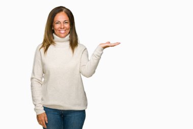 Neşeli sunulması ve kameraya bakarak avucunun ile işaret gülümseyen izole arka plan üzerinde kış kazak giyen güzel orta yaş yetişkin kadın.