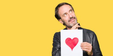 Kırmızı kalp ciddi bir yüz düşünce hakkında soru, çok karışık bir fikir ile kağıt tutan yakışıklı orta yaş erkek