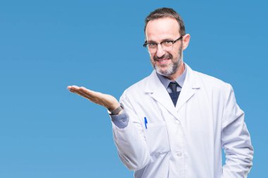 Orta yaş üst düzey ağarmış profesyonel adam neşeli sunulması ve kameraya bakarak avucunun ile işaret gülümseyen izole arka plan üzerinde beyaz önlük giyiyor.