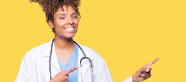 Genç Afro-Amerikan doktor kadın gülümseyerek ve iki elleri ve parmakları ile tarafına işaret kamera bakarak izole arka plan.