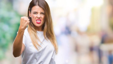 Genç güzel kadın rahat beyaz t-shirt üzerine arka plan öfkeli ve sinirli sinirli ve öfke ile bağırarak süre öfkeli yumruk yükselterek izole. Öfke ve agresif kavramı.