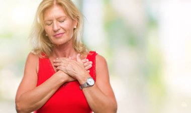 Orta yaş sarışın kadın ile gülümseyen izole arka plan yüzünden kapalı gözler ve yüzünde minnettar jest ile göğüs üzerinde eller. Sağlık kavramı.