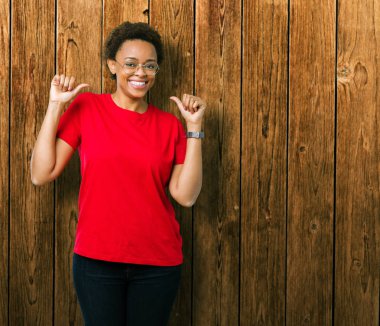 Güzel genç Afro-Amerikan kadın yüzünde gülümseme ile kendinden emin görünüyorsun, kendini gururlu ve mutlu parmakları ile işaret izole arka plan üzerinde gözlük.