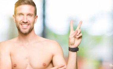 Gömleksiz yakışıklı gösteren çıplak göğüs mutlu yüz zafer işareti yaparken kameraya göz kırpıyor ile gülümseyen. İki numaralı.