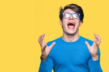 Üzerinde mavi gözlük takan genç yakışıklı adam arka plan deli izole ve deli bağırarak ve agresif ifade ve silah kaldırdı bağırıyor. Hayal kırıklığı kavramı.