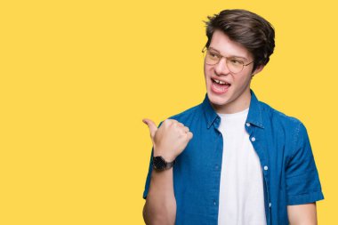 Seyir ve başparmak yanında yukarıyı mutlu yüz ile gülümseyen izole arka plan üzerinde gözlük takan genç yakışıklı adam.