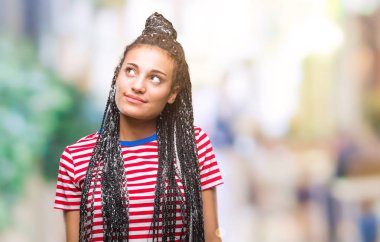 Genç saç Afro-Amerikan Kız görünümlü yan ve dik dik bakma uzağa düşünce gülümseyen izole arka plan üzerinde örgülü..