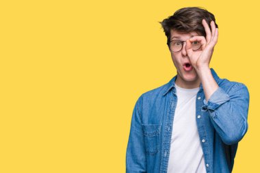 Sürpriz yüz, göz parmaklarının arasından seyir ile ok jest yapıyor izole arka plan üzerinde gözlüklü genç yakışıklı adam şok. İmansız ifade.