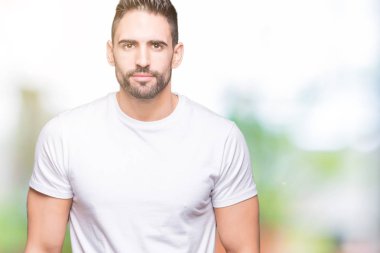 Üzerinde rahat beyaz t-shirt giyen genç adam arka plan gevşek yüzünde ciddi bir ifade ile izole. Basit ve doğal kameraya bakıyor.