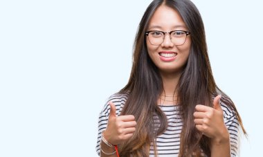El ile pozitif jest yapıyor izole arka plan başarı işareti üzerinde gözlük takan Genç Asyalı kadın başparmak gülümseyen ve mutlu. Neşeli bir ifadeyle, kazanan jest kameraya bakıyor.