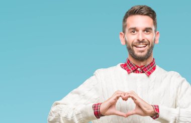 Genç yakışıklı adam aşık kalp simgesi ve elleriyle şekil gösteren gülümseyen izole arka plan üzerinde kış kazak giyiyor. Romantik kavramı.