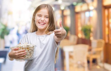 Genç güzel kız ok işareti, başparmak ile parmak, mükemmel işareti yapıyor kocaman bir gülümseme ile patlamış mısır snack izole arka plan mutlu yemek