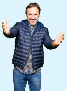 Orta yaş yakışıklı adam sarılmak için kollarını açarak gülümseyerek kameraya bakarak kış palto giyiyor. Neşeli ifade kucaklayan mutluluk.