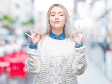 Sarışın genç kadın giyiyor kış kazak izole arka plan üzerinde dinlenmek ve gülümseyen gözlerle kapalı parmak jestle meditasyon yapıyor. Yoga kavramı.