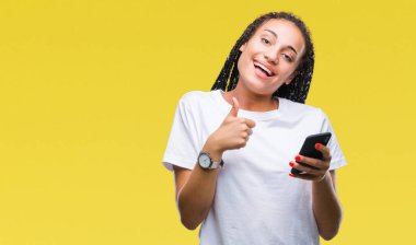 Genç örgülü saç Afro-Amerikan Kız gösterilen ok işareti yapıyor büyük gülümseme ile izole arka plan üzerinde mutlu smartphone kullanarak başparmak yukarı parmaklarıyla, mükemmel işareti