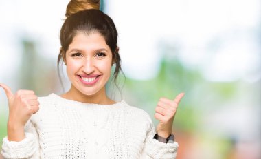 Kış kazak başarı işareti el ile pozitif jest yapıyor giyen genç güzel kadın başparmak gülümseyen ve mutlu. Neşeli bir ifadeyle, kazanan jest kameraya bakıyor.