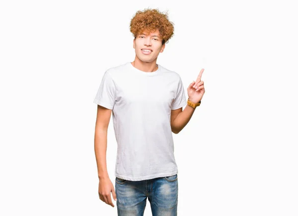 カメラを見て側に手と指で指しているアフロ髪の顔に大きな笑みを浮かべて白い シャツ カジュアルを着ている若いハンサムな男 — ストック写真