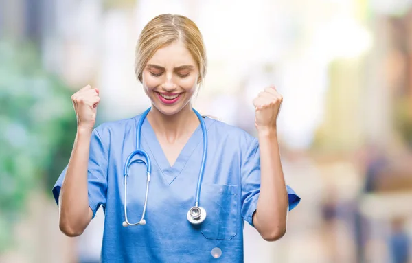 年轻美丽的金发医生外科医生护士妇女在孤立的背景兴奋为成功与胳膊上升庆祝胜利微笑 优胜者概念 — 图库照片