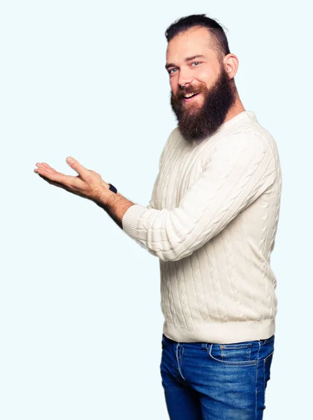年轻的嬉皮士男子穿着冬季毛衣指着身边的手和开放的手掌 呈现广告微笑的快乐和自信 — 图库照片