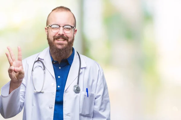 年轻的高加索医生男子穿着医疗白色外套在孤立的背景显示和手指第三 而微笑着自信和快乐 — 图库照片