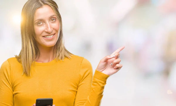 年轻的美丽的女人发送消息使用智能手机在孤立的背景非常高兴用手和手指指向一边 — 图库照片