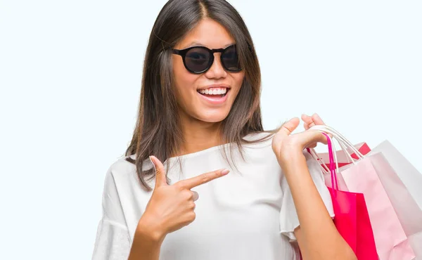 年轻的亚洲妇女拿着购物袋在销售结束孤立的背景非常高兴地指着手和手指 — 图库照片