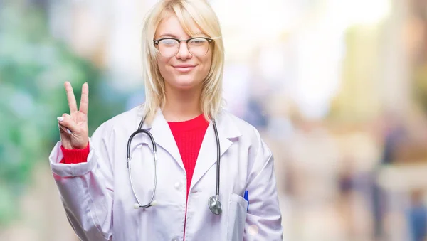年轻美丽的金发医生妇女穿医疗制服在孤立的背景显示和指向与手指第二 微笑自信和快乐 — 图库照片