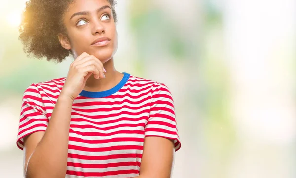 Young afro american woman over isolated background with hand on chin thinking about question, pensive expression. Smiling with thoughtful face. Doubt concept.