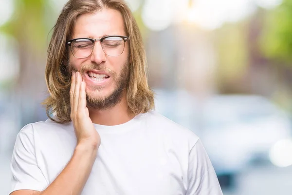 Young handsome man with long hair wearing glasses over isolated background touching mouth with hand with painful expression because of toothache or dental illness on teeth. Dentist concept.