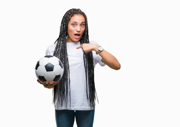 年轻的编织头发非洲裔美国女孩拿着足球在孤立的背景与惊喜的脸指向自己的手指 — 图库照片