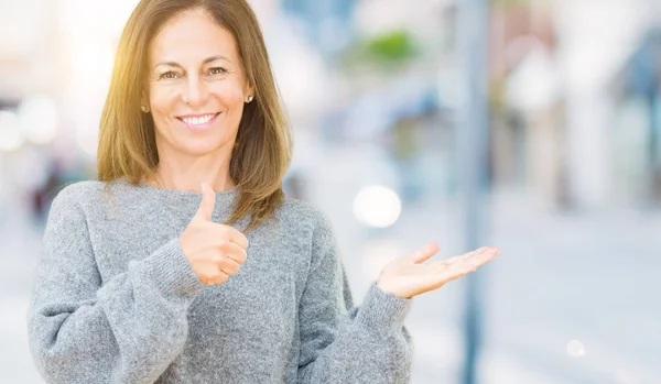 上冬のセーターを着て美しい中年女性分離背景幸せで陽気な笑みを浮かべて親指を示すパーム手でやって ジェスチャー — ストック写真