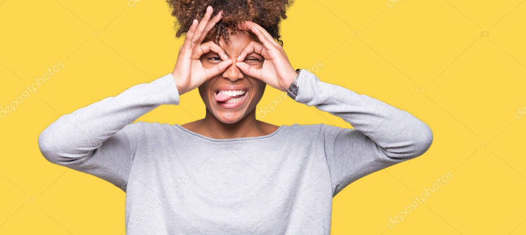 Beautiful young african american woman over isolated background doing ok gesture like binoculars sticking tongue out, eyes looking through fingers. Crazy expression.
