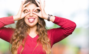 Kırmızı kazaklı, dilini parmaklarının arasından baktığını yapışmasını dürbün gibi ok jest yapıyor giyen genç güzel kadın. Deli ifade.