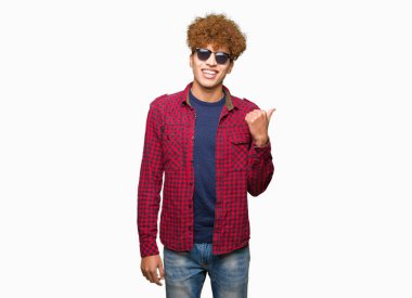 Seyir ve başparmak yanında yukarıyı mutlu yüz ile gülümseyen güneş gözlüğü takıyor afro saçlı Genç yakışıklı adam.