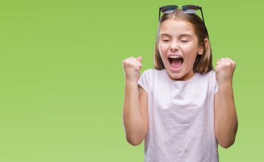 Genç güzel kız izole arka plan kutlama üzerinde güneş gözlüğü takıyor şaşırttı ve başarı için kaldırdı kollarını açarak hayret ve gözleri açık. Kazanan kavramı.