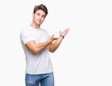 Açık el ile doğal gülümseyen girmek için davet izole arka plan üzerinde beyaz t-shirt giyen genç yakışıklı adam