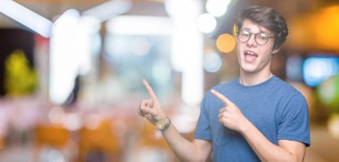 Gülümseyen ve iki elleri ve parmakları ile tarafına işaret kamera bakarak izole arka plan üzerinde gözlük takan genç yakışıklı adam.