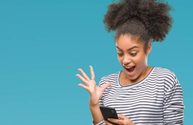 Genç afro Amerikalı kadın manifatura üzerinden Smartphone kullanarak büyük gülümseme ile çığlık zaferini kutluyor arka plan çok mutlu ve heyecanlı, kazanan ifade izole ve ellerini kaldırdı