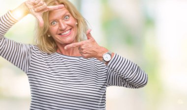 Orta yaş sarışın kadın elle yapma çerçeve ve parmakları ile mutlu yüz gülümseyen izole arka plan yüzünden. Yaratıcılık ve Fotoğrafçılık kavramı.