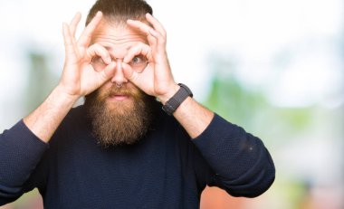 Gözlük ve dilini, parmaklarının arasından baktığını yapışmasını dürbün gibi ok jest yapıyor boğazlı kazak giyen genç sarışın adam. Deli ifade.