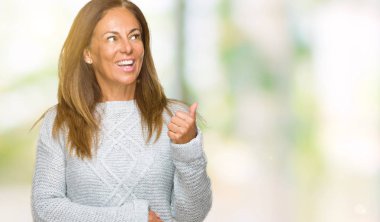 Seyir ve başparmak yanında yukarıyı mutlu yüz ile gülümseyen izole arka plan üzerinde kış kazak giyen güzel orta yaş yetişkin kadın.